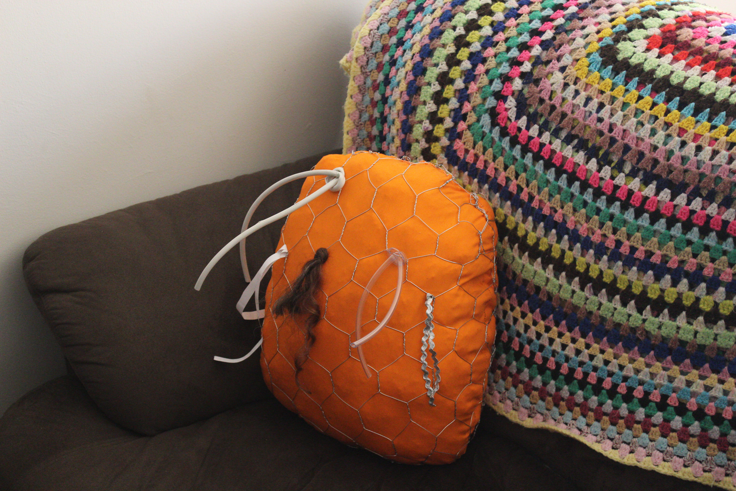 Orange soft sculpture sitting on brown couch with crocheted blanket