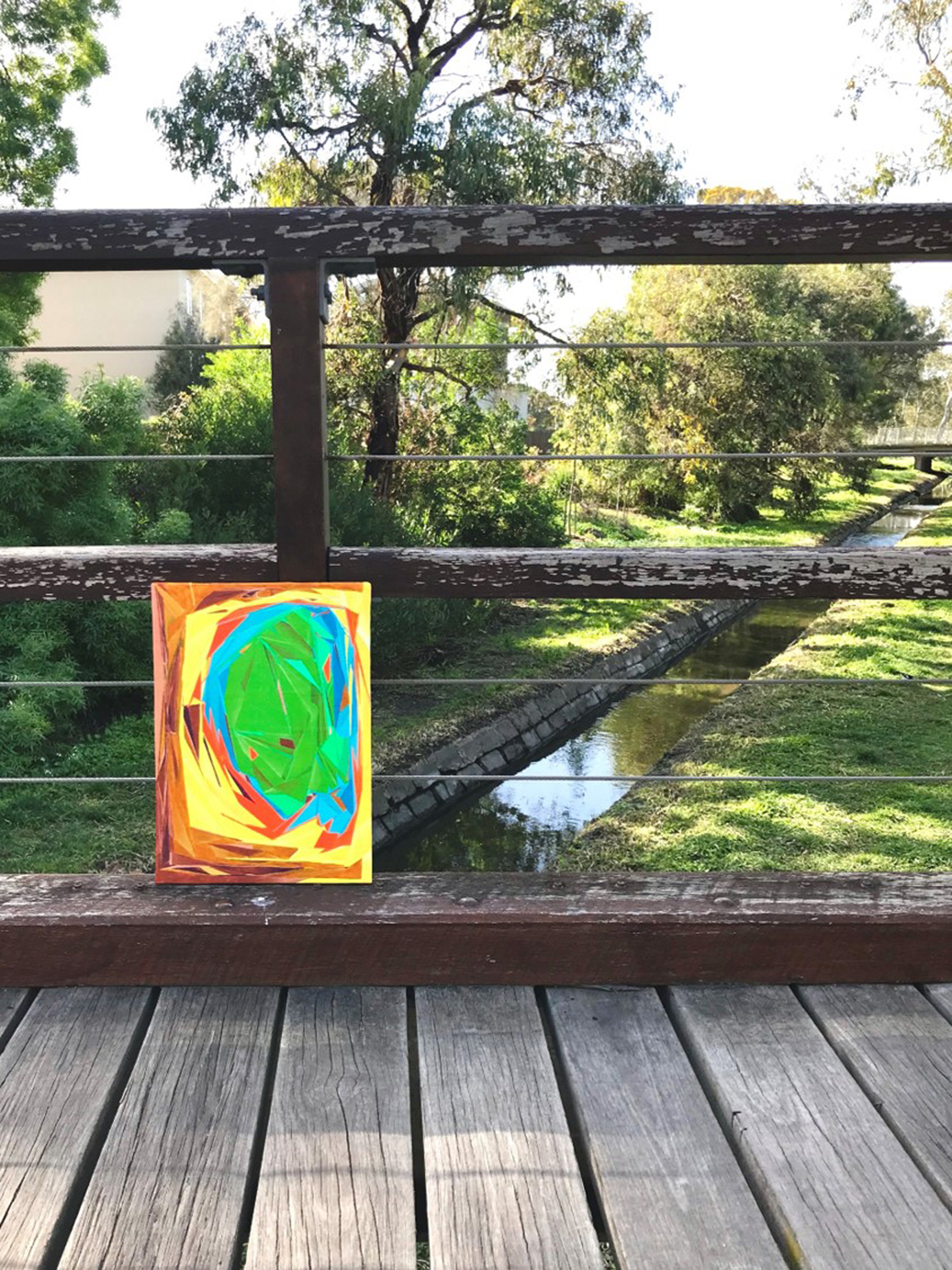 A digital photograph of the installation of the painting titled "Not Pretending Anything" located on a bridge in a nature reserve and featuring a narrow canal.