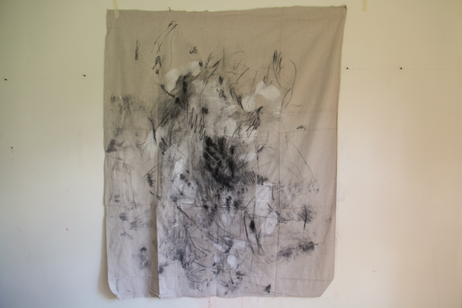 Fragmented figurative black and white charcoal drawing on fabric, one hand is visible the rest of the fabric is covered in marks and smudges