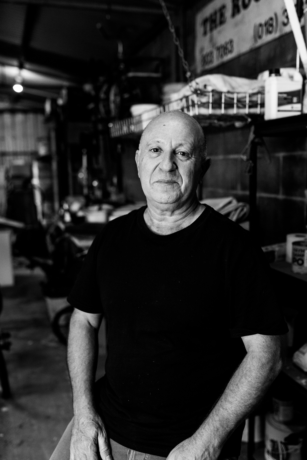 Black and white photograph of a portrait of an man sitting in a garage.