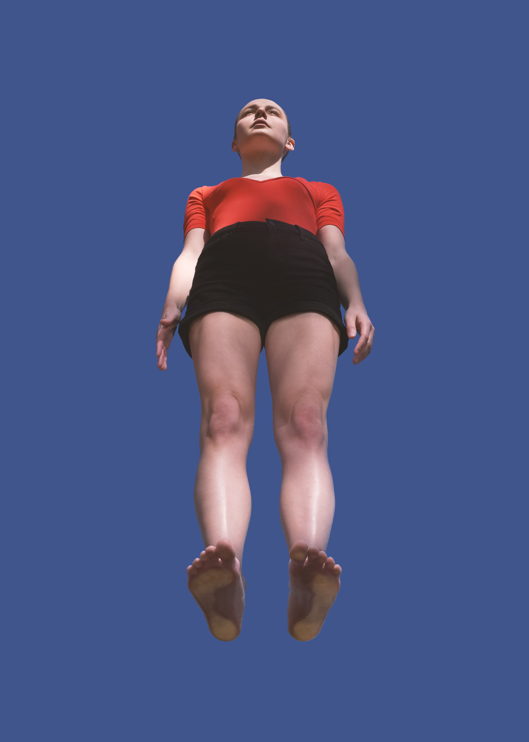Colour video still of woman in red top and black shorts. Woman stand on perspex as video is taken from below.