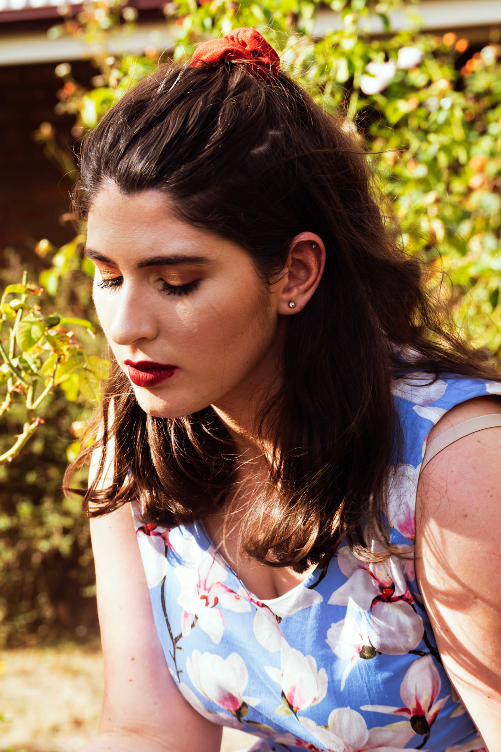 Colour photograph of closeup portrait of attractive brown-haired female in dress in garden in golden light.