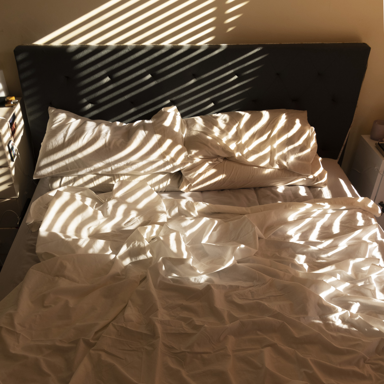 Colour photograph of empty bed with messy sheets bathed in golden light.