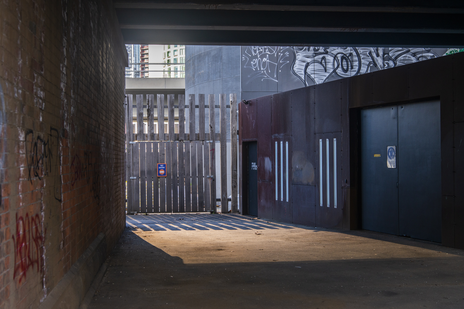 Colour photograph of light entering through a narrow gap between city buildings. 
