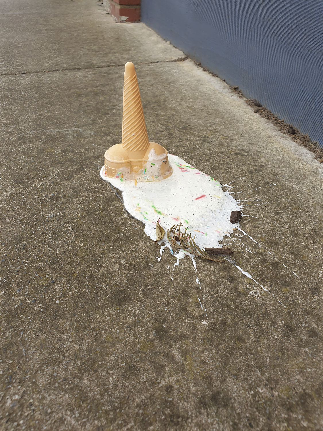 Colour photograph of upside down ice cream cone on melting ice cream on footpath.