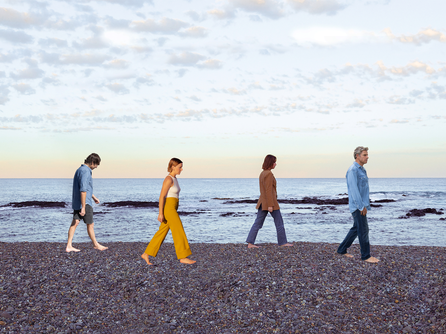 Colour image of four people walking consecutively in a line along a shore line. 