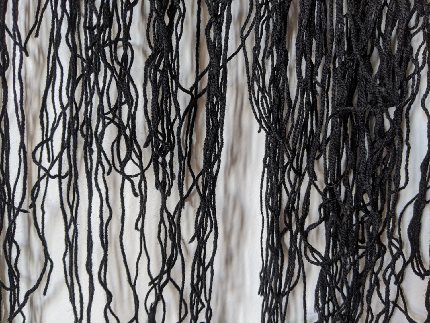 Close up/texture detail of black yarn threads hanging from coat hanger
