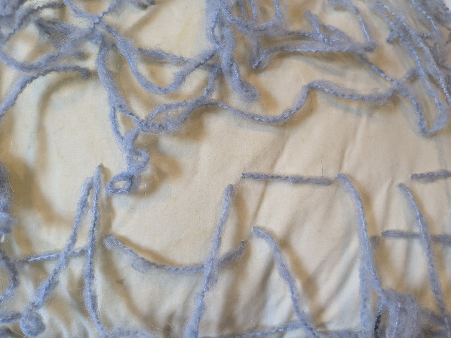 Close up of a yellowing pillow background and lines composed of with wispy blue yarn