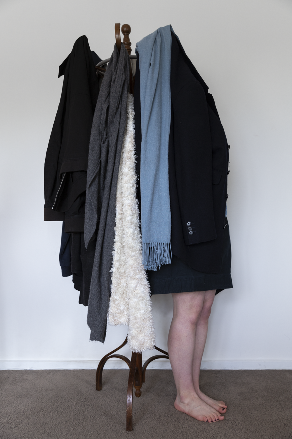 Colour photograph of coat rack against white wall with two legs sticking out from the coats.