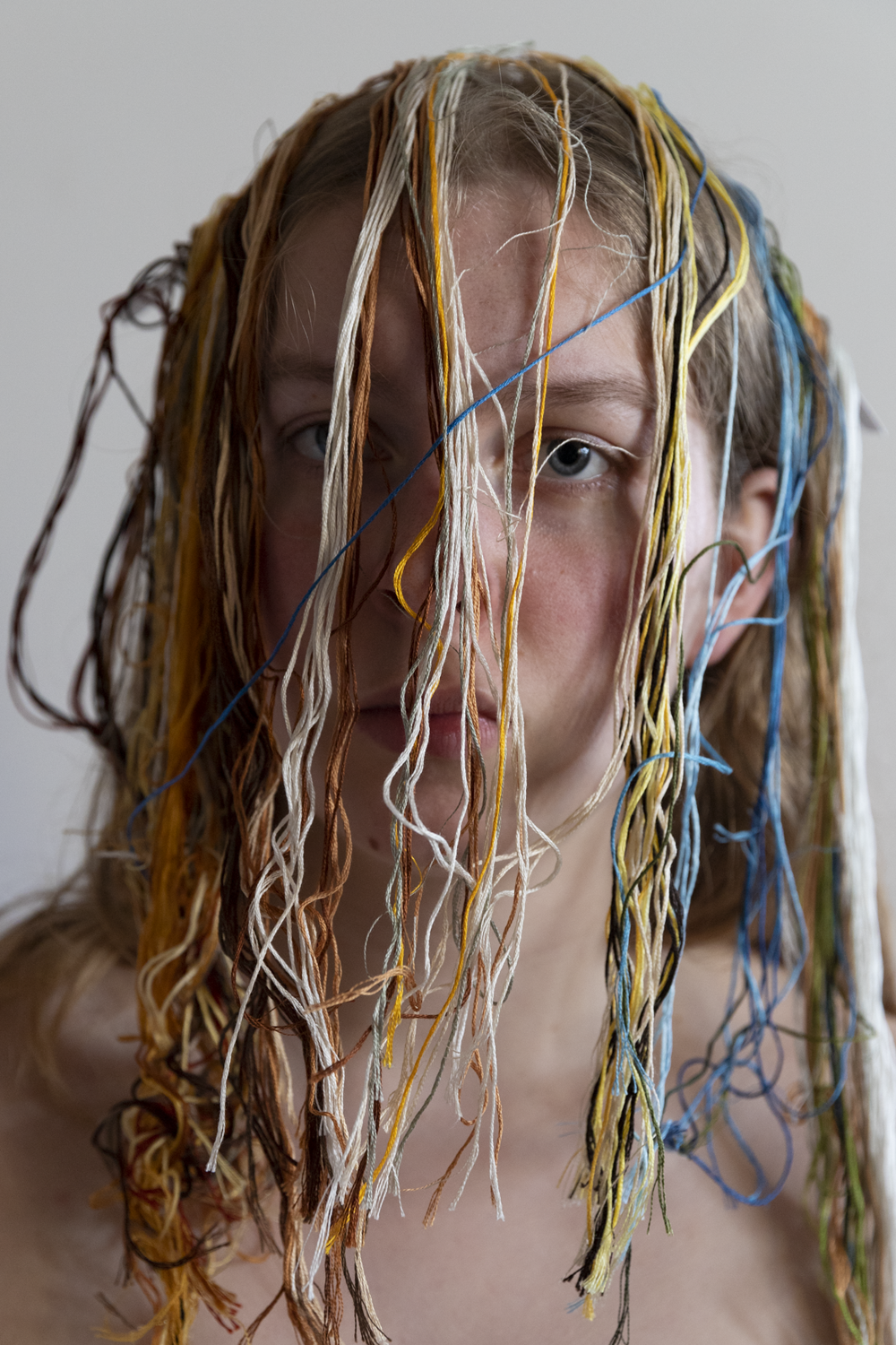 Colour photograph of female face covered with multicoloured strings.