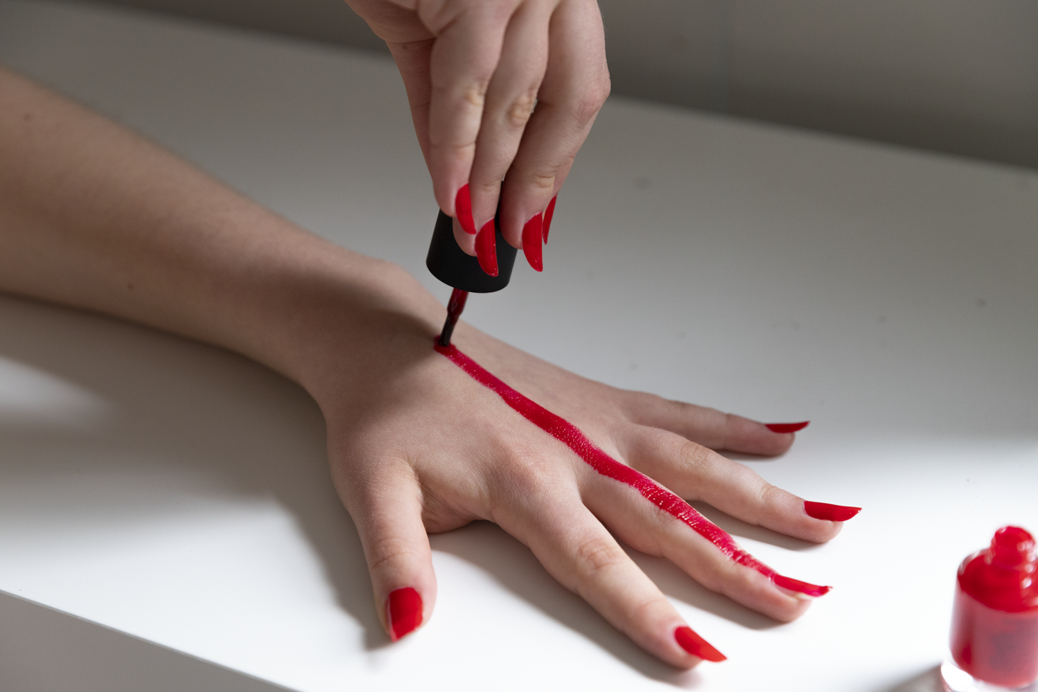 Colour photograph of hand being painted with red nail polish.