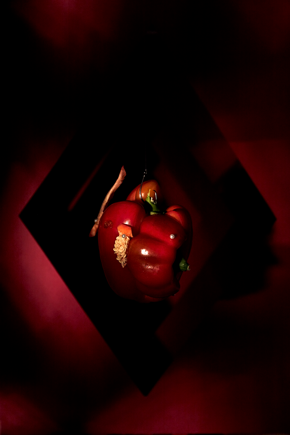 Colour photograph of capsicum hanging in a red diamond formation in red dappled light.