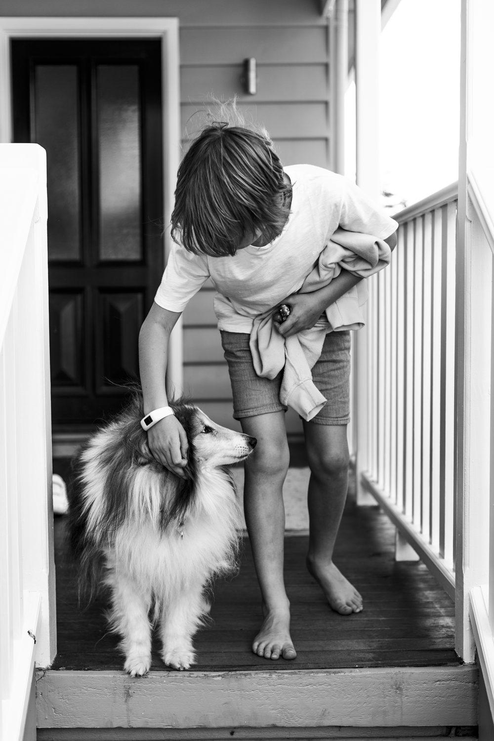 Black and white photograph of a portrait of a young boy with a dog on a domestic veranda.