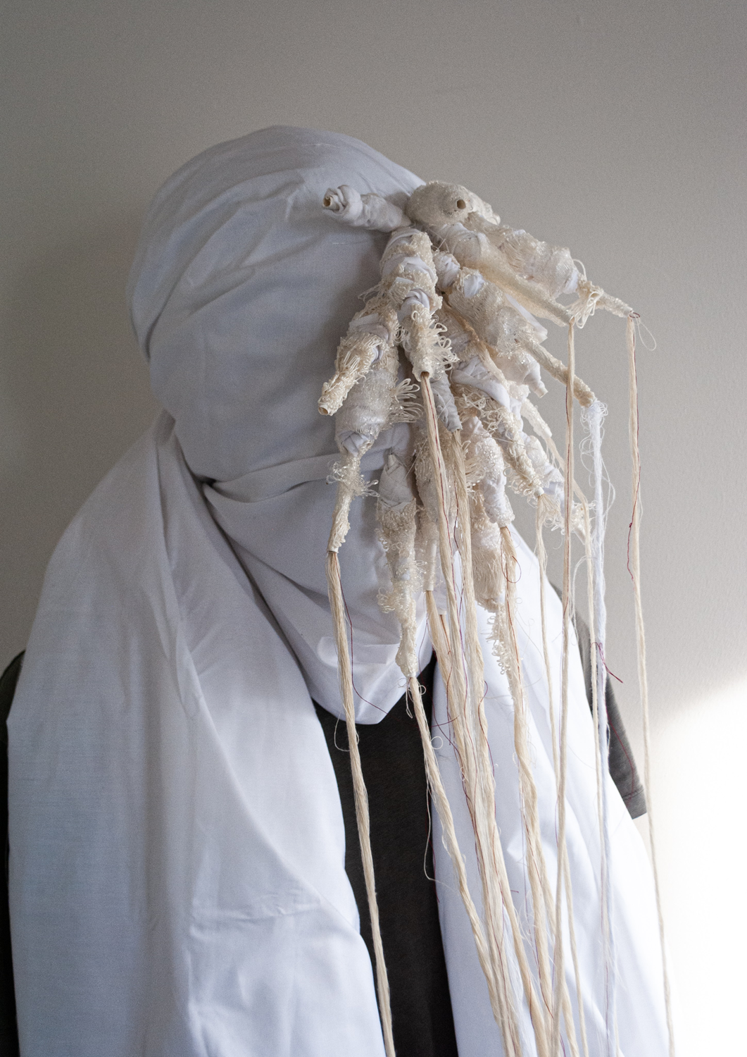 figure wearing white cloth hood and mask with threads