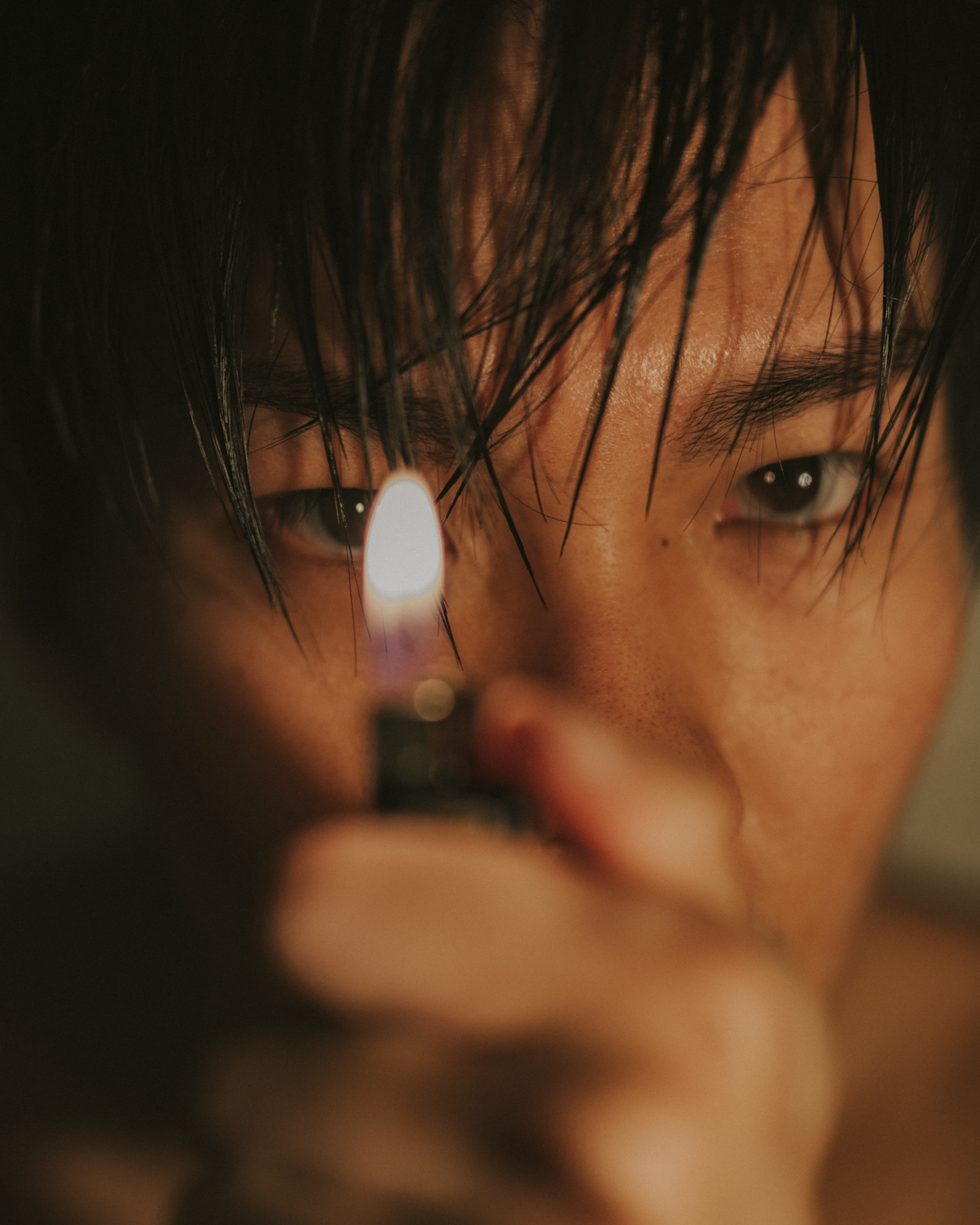 Colour photograph of moody and tightly framed self-portrait of artist with a lit lighter illuminating face.