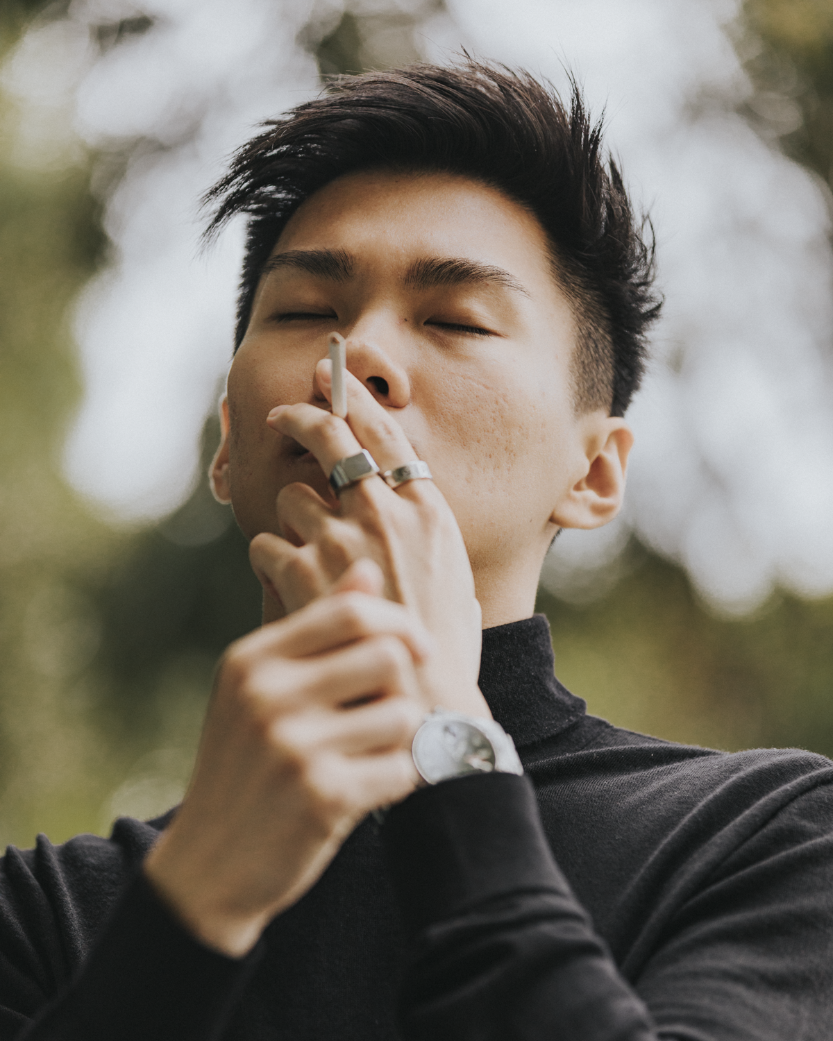 Colour photograph of a self-portrait of the artist placing an unlit cigarette in their mouth as they clutch their wrist in an outdoor environment.