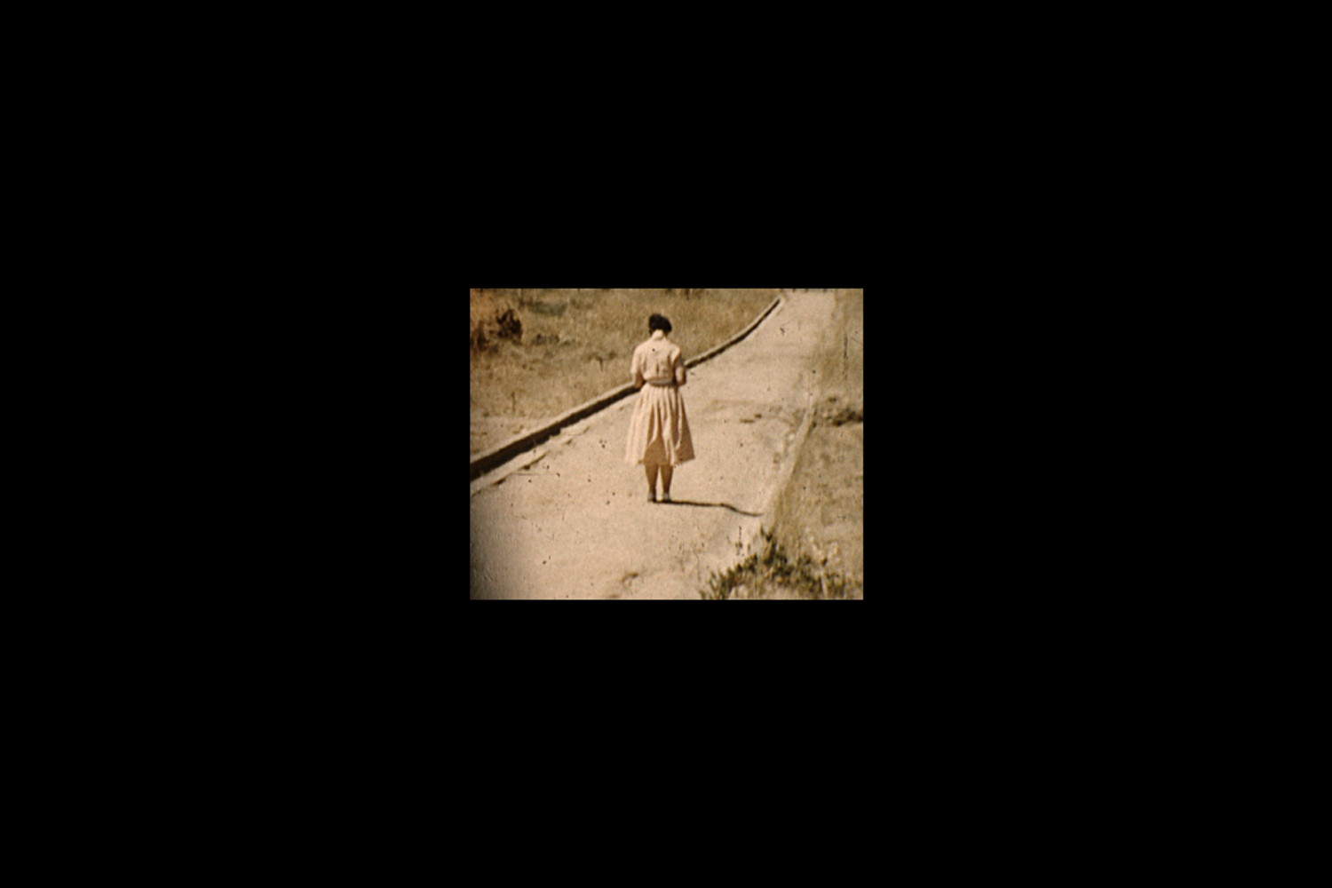 Colour photograph depicting a projected archival sepia image of a woman standing on a dirt path.