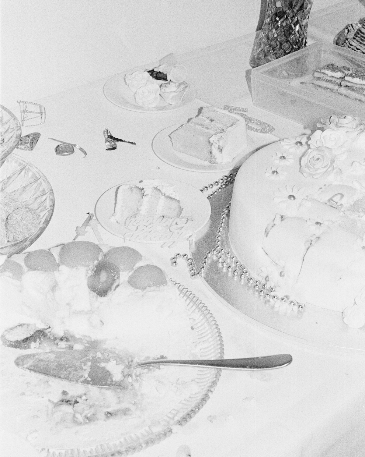 Colour photograph depicting black and white image of table with white cloth and half eaten cake.