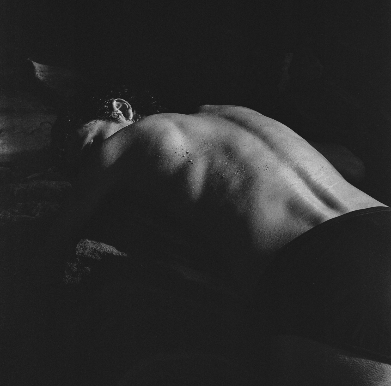 Black and white photograph depicting man's back in sunlight.