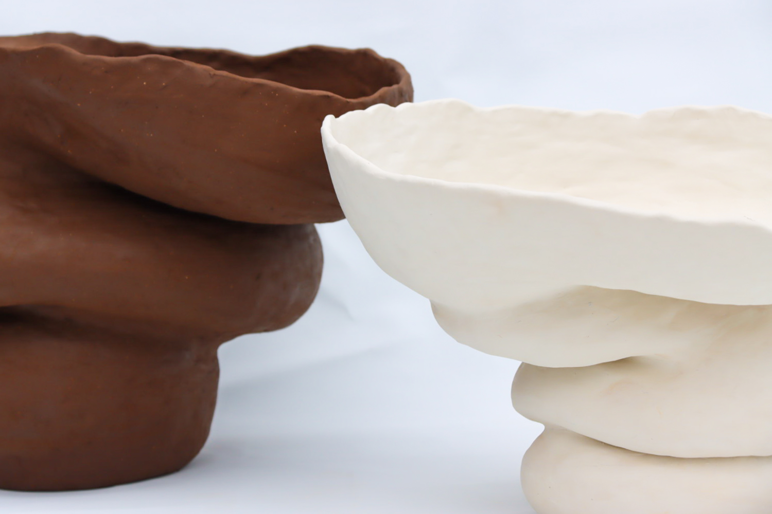 Close up image of two large voluptuous ceramic forms lined up in front of a white backdrop, coloured from left to right, dark brown and white.
