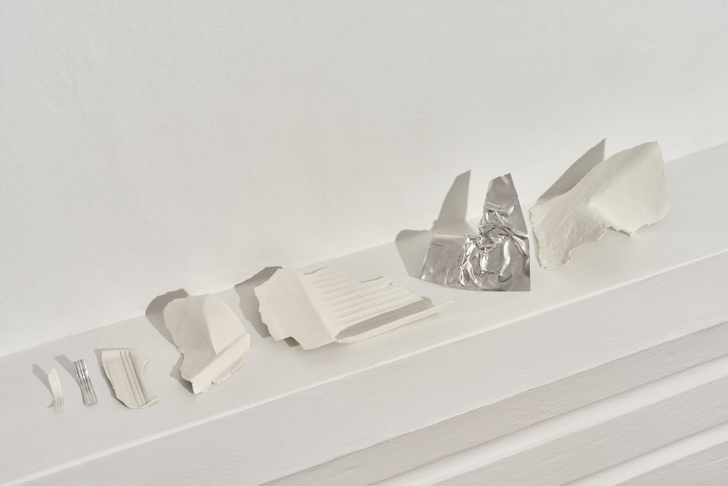 Collection of clay and aluminium fragments displayed in line on mantle piece 