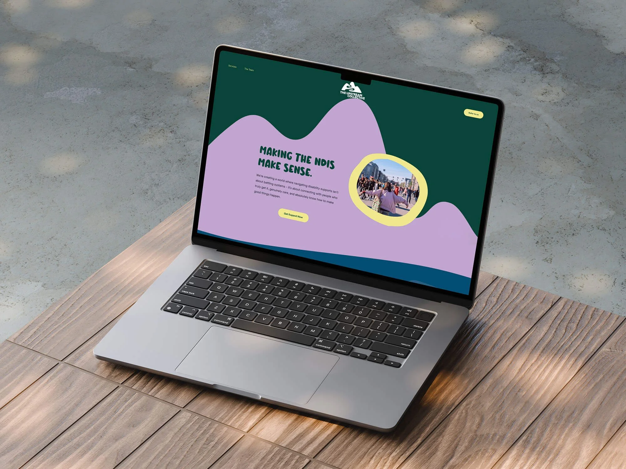 A screenshot of the home page for previous KGD client, The Upstream Collective on a laptop screen, sat outdoors on a wooden table.