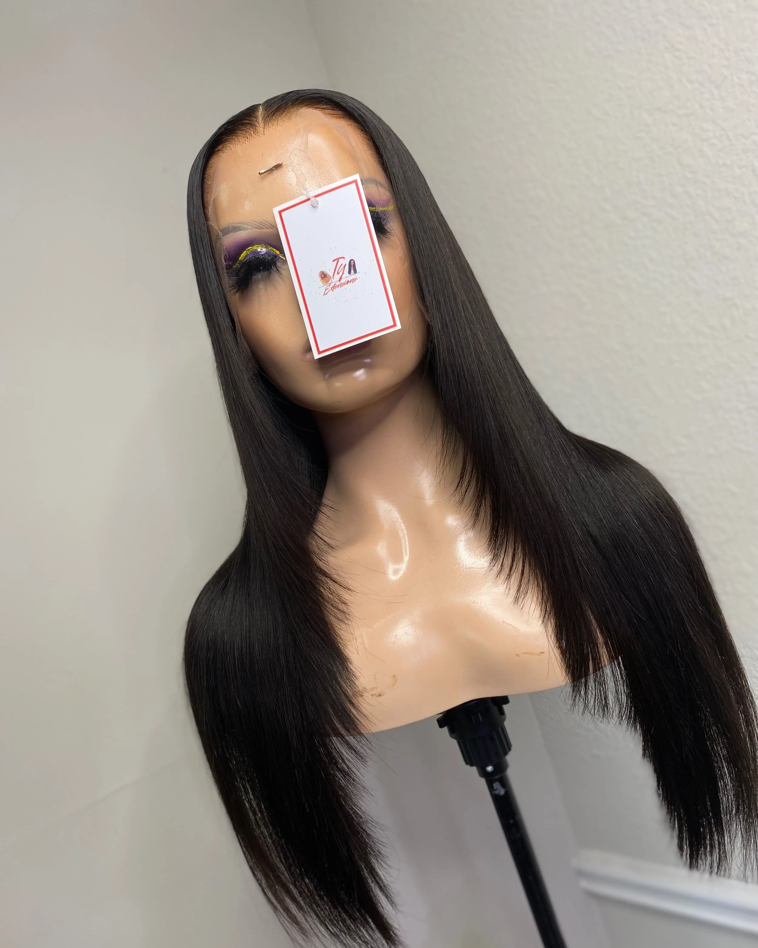Mannequin head with long straight black hair and colorful makeup, on a stand, with a tag hanging from the forehead.