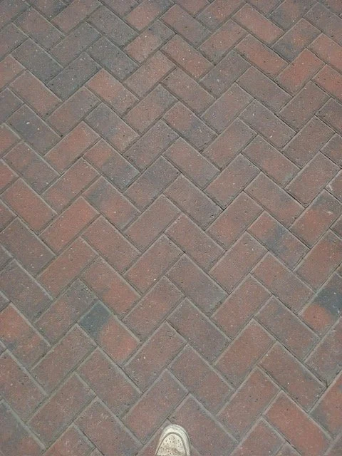 Close-up of brick sidewalk with a person's sneaker visible at the bottom edge.