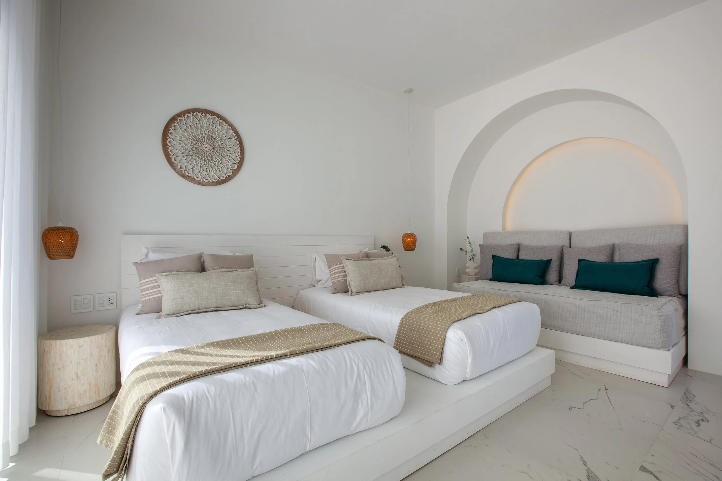 A bedroom with two beds and a sofa, featuring neutral and teal color accents, white walls, and decorative wall art.