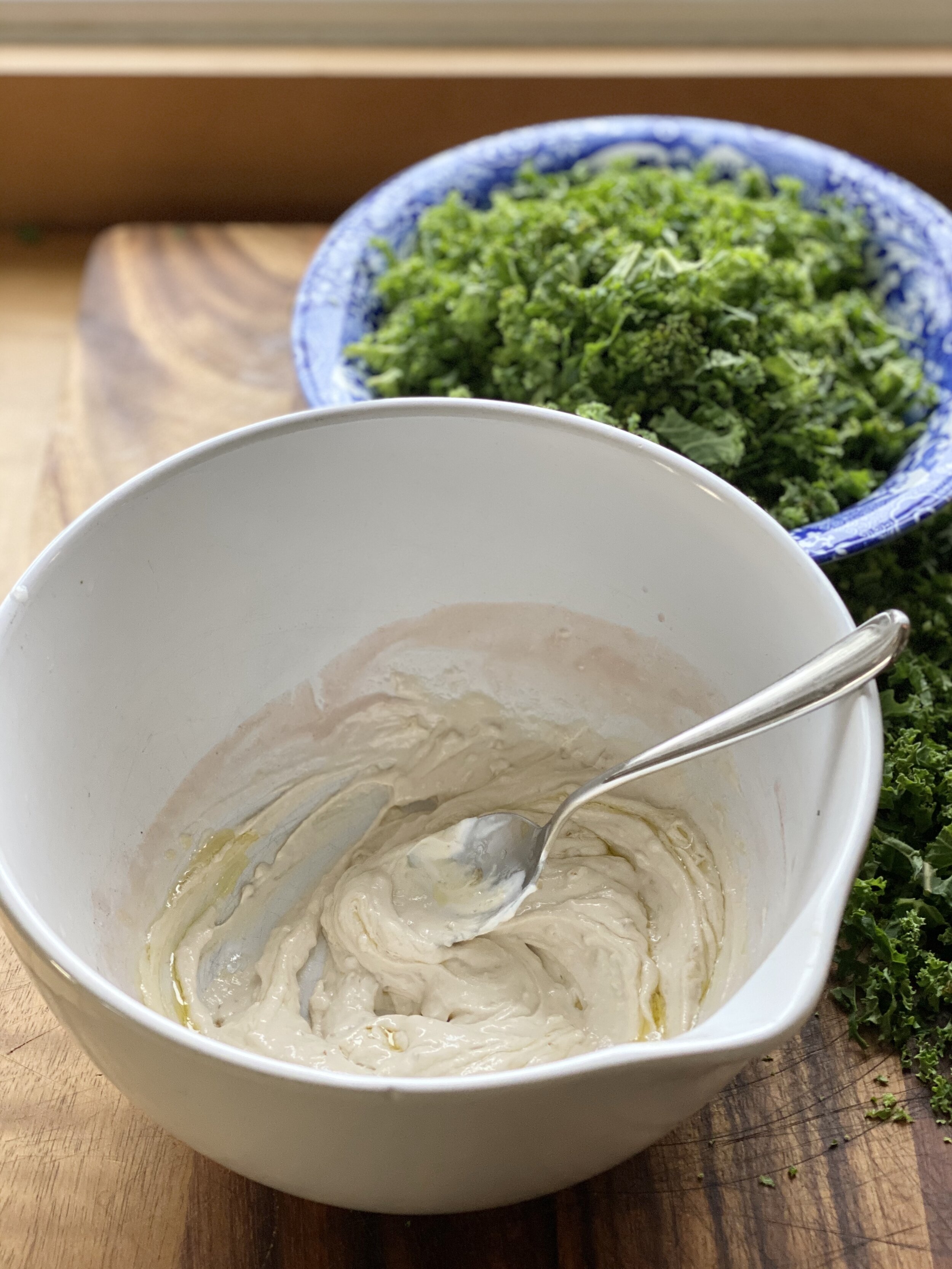 Yogurt tahini dressing mixed with a spoon in a white bowl