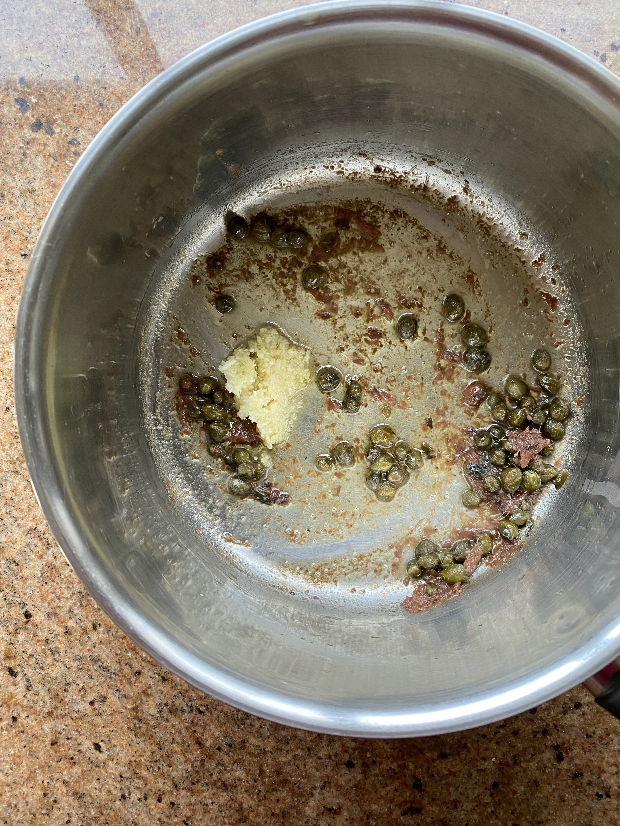 Garlic, anchovies and capers frying gently in olive oil in a small saucepan