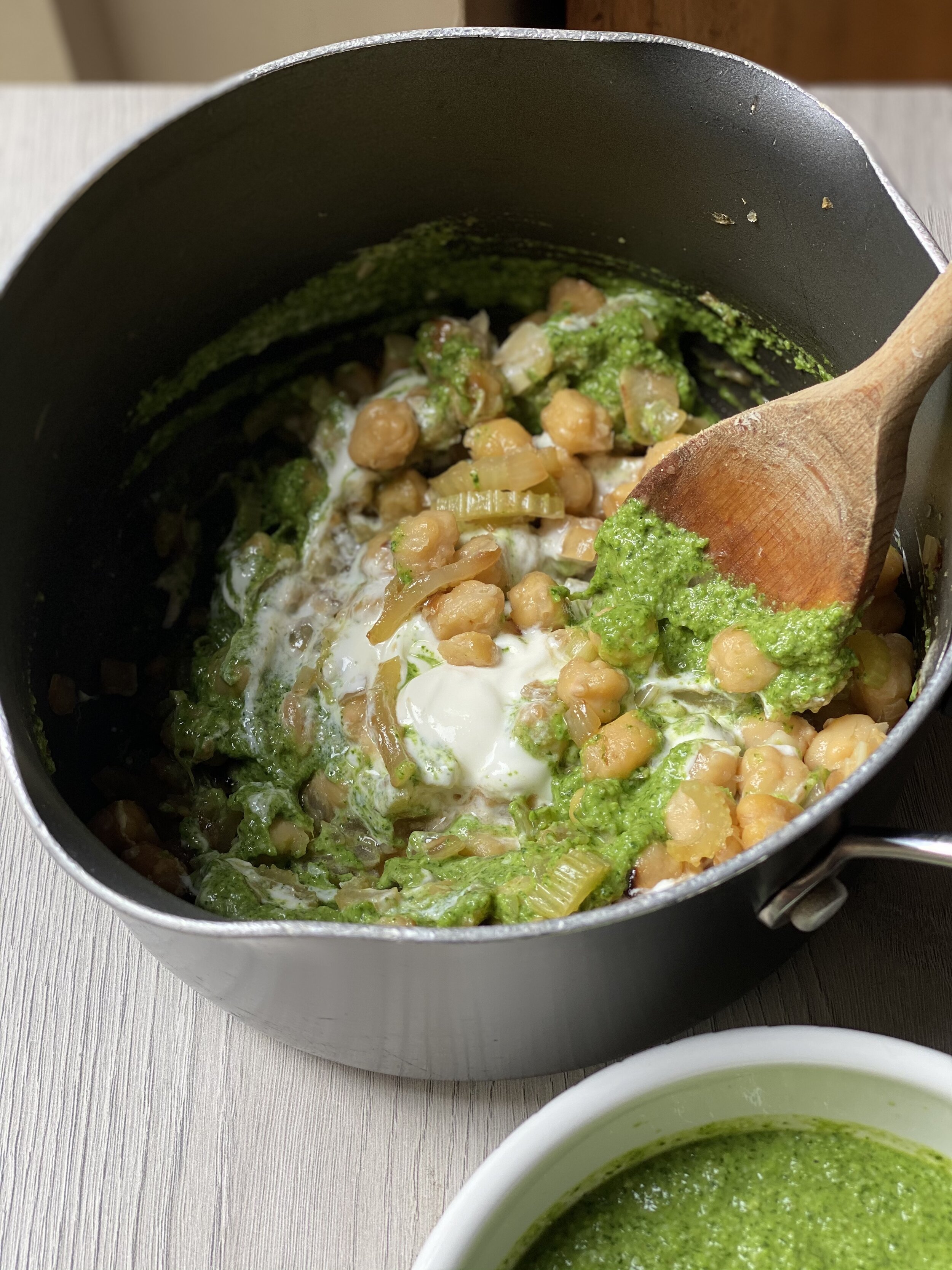 Creamy chickpeas being stirred with watercress pesto