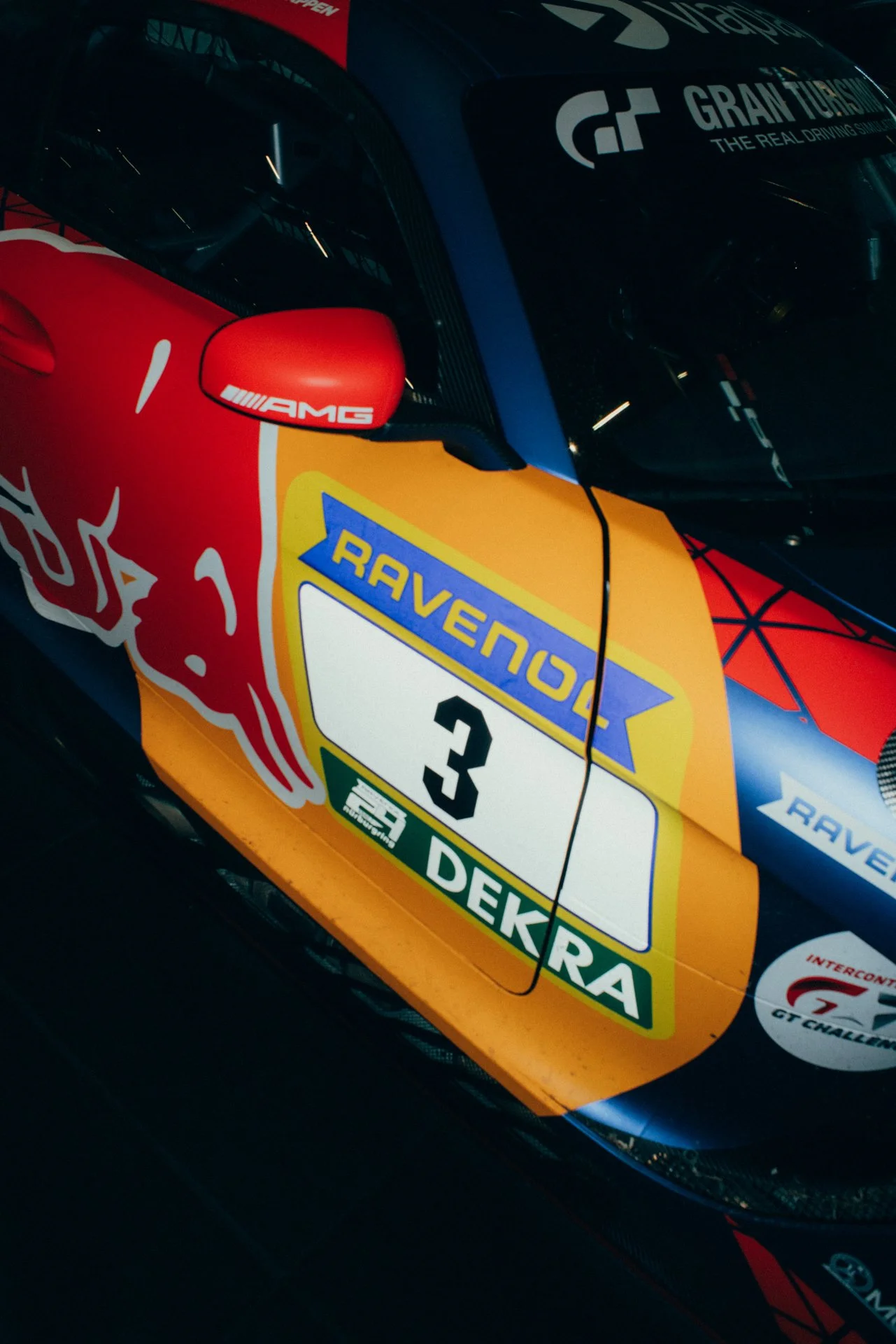 Close-up of a race car's side with championship and sponsor logos, number 3, and a Red Bull logo, featuring a colorful design with red, yellow, blue, and green accents.