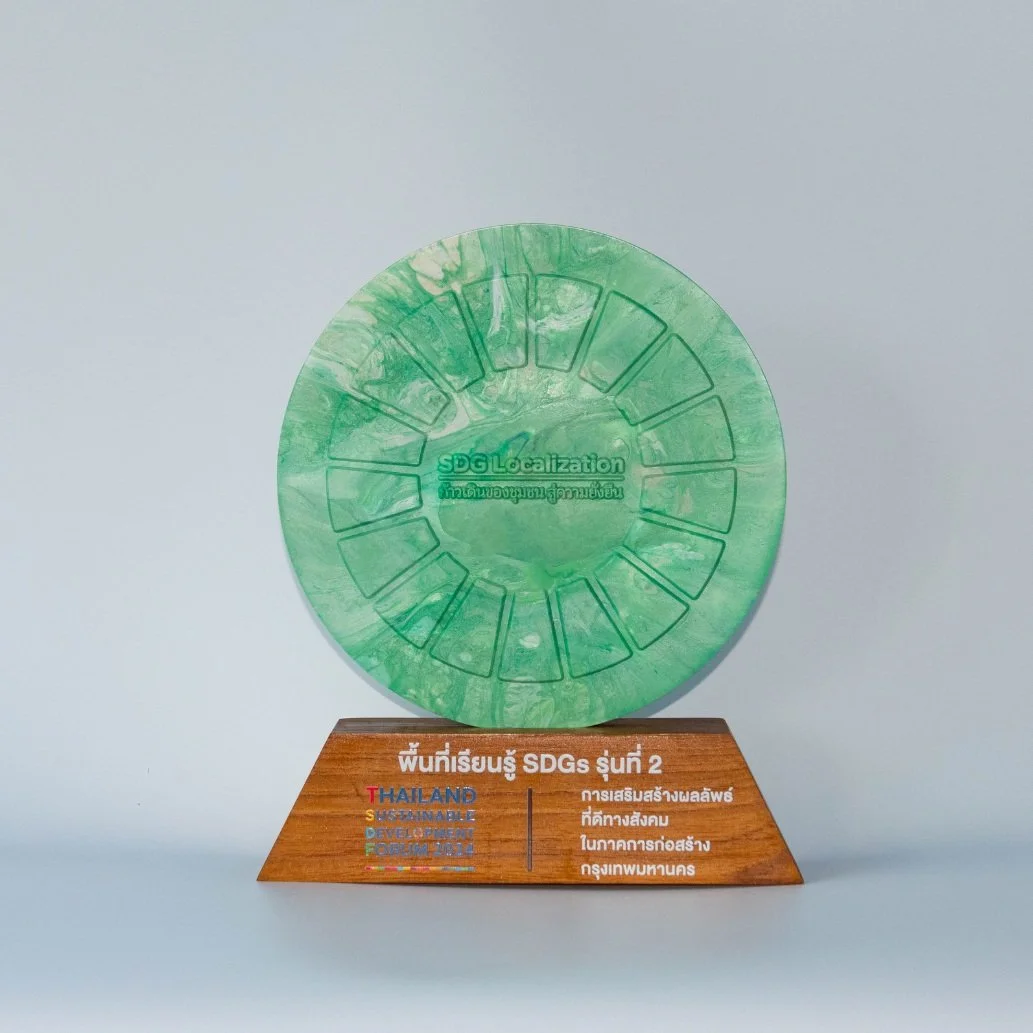 A green circular award with the words 'SDG Localization' on the front, mounted on a wooden base that has text in Thai and English about sustainable development goals in Thailand.
