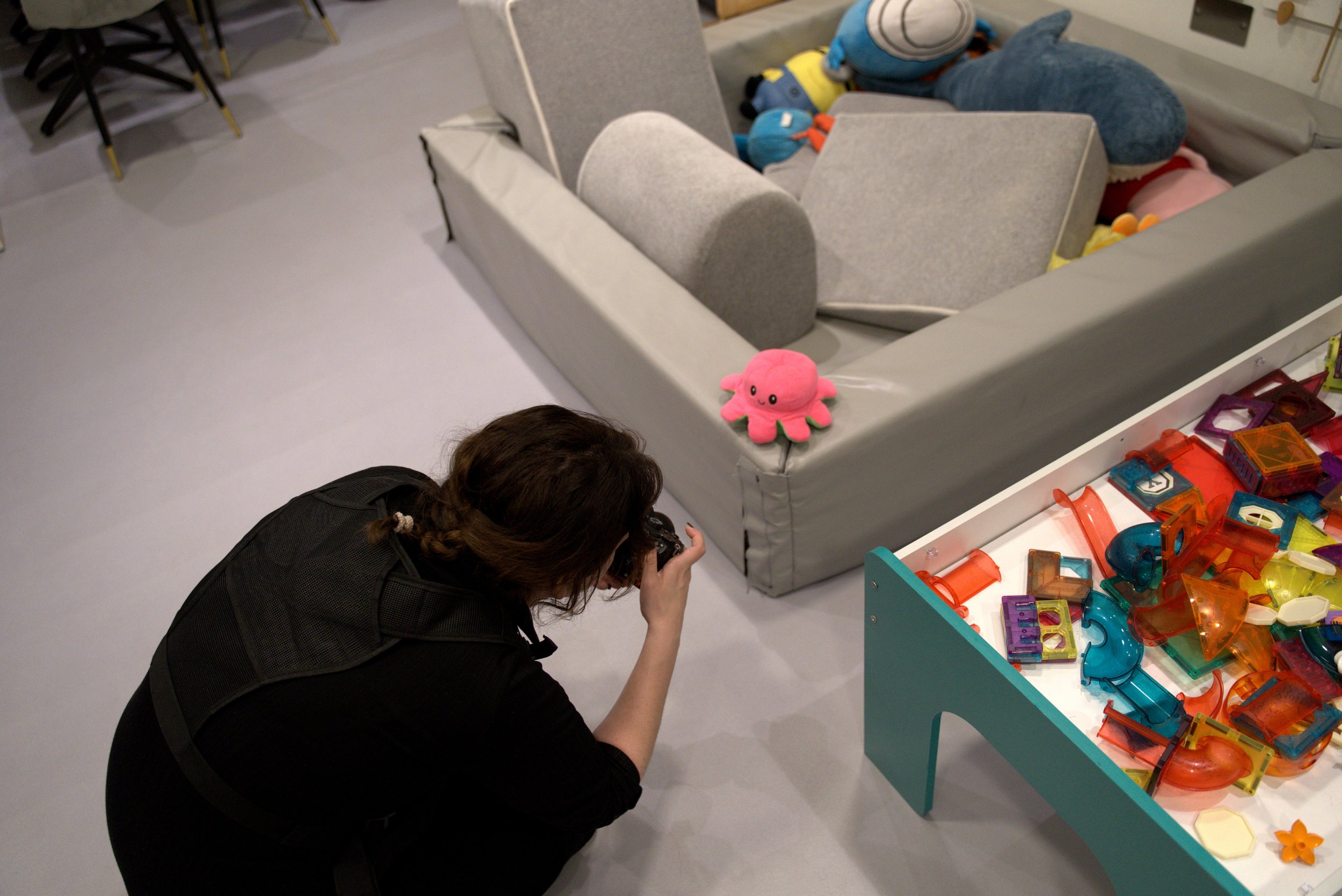 Person photographing toys in a play area with stuffed animals and colorful plastic blocks.