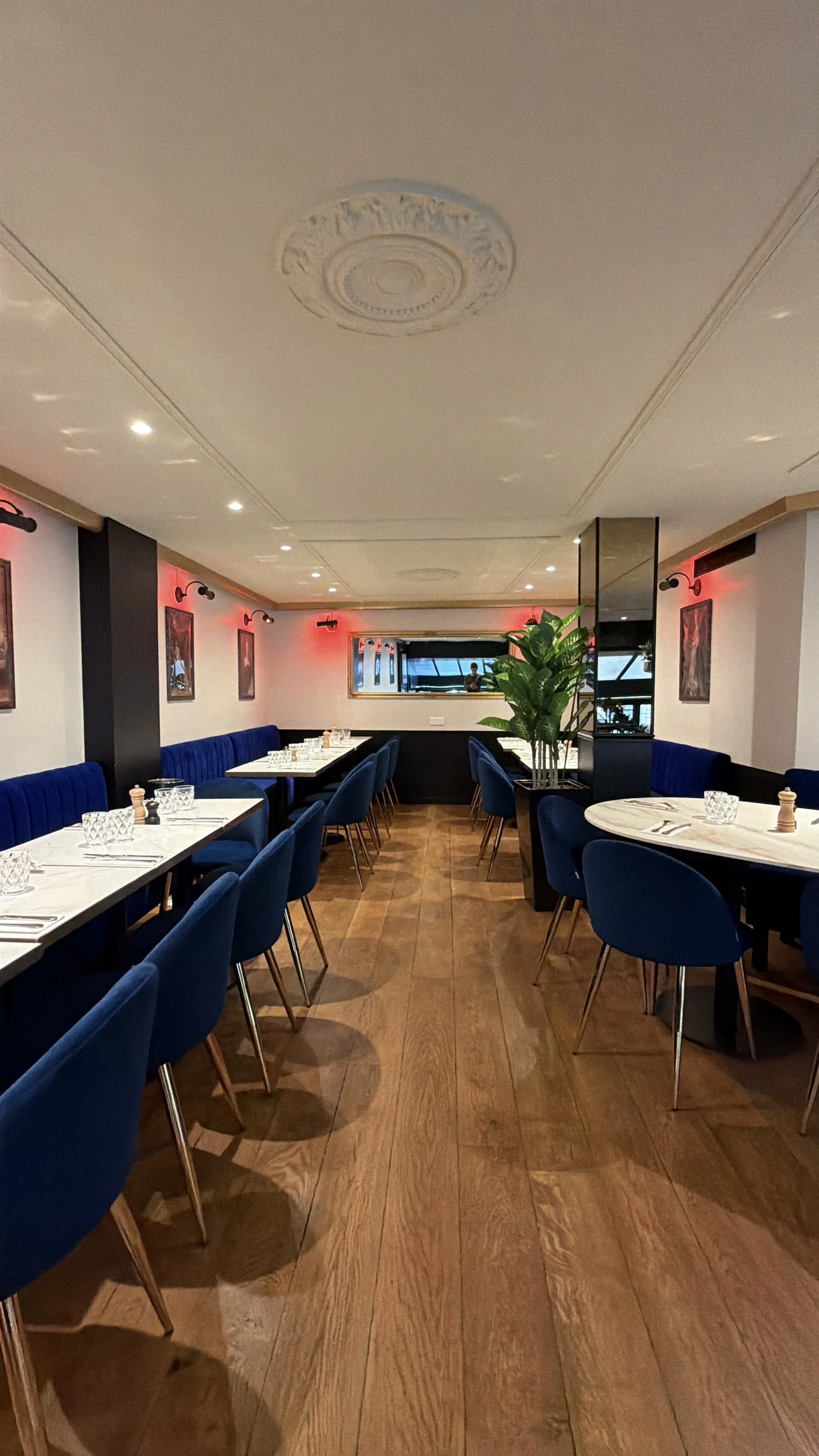 Elegant restaurant interior with tables covered in white tablecloths and chandeliers, walls decorated with portraits, ceiling adorned with motifs.
