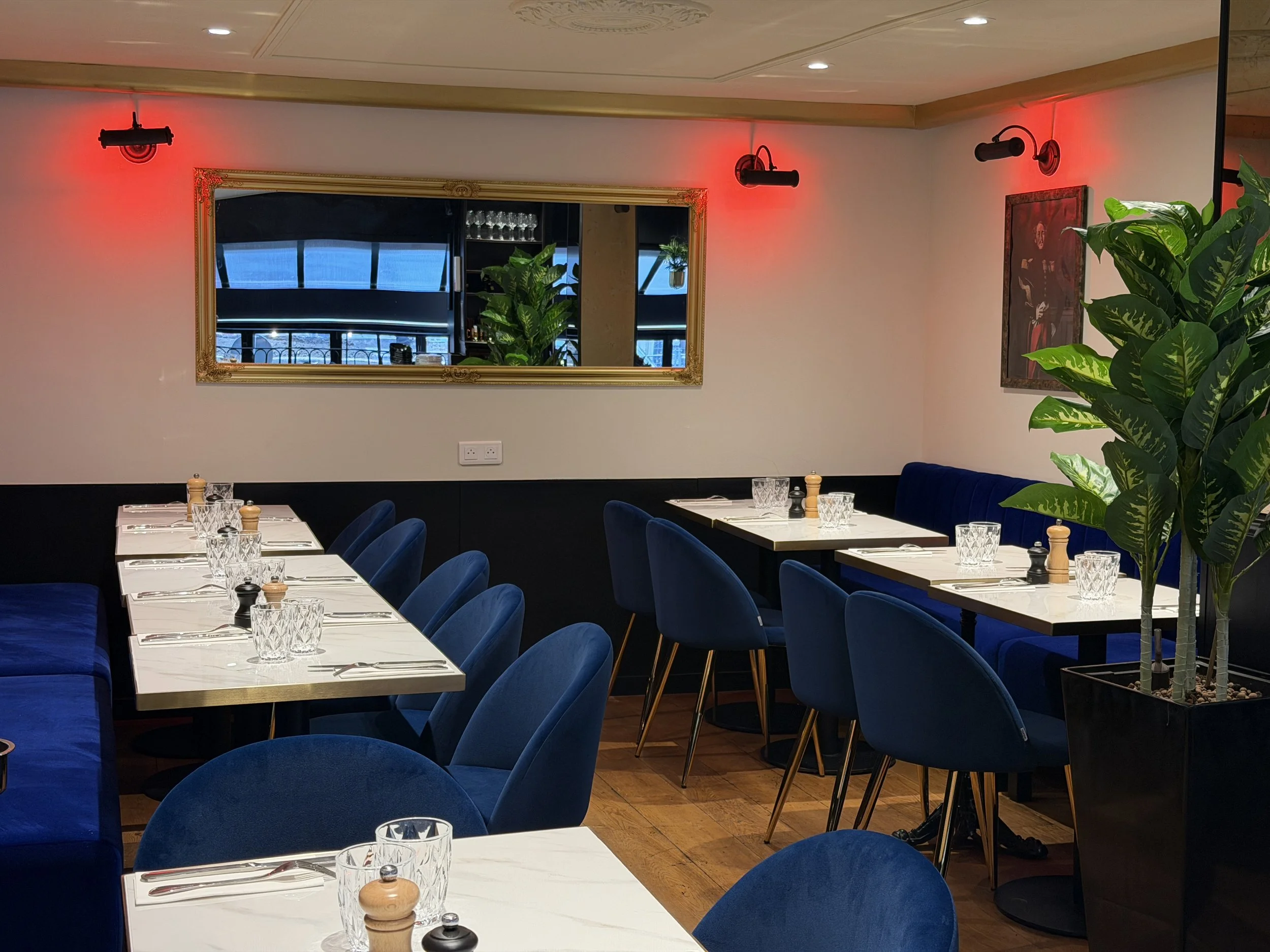 Elegant restaurant interior with set tables, brown chairs, white tablecloths, wine glasses, plants and paintings on the walls.
