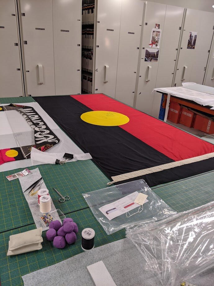 Laying the flag on top of a support lining, in preparation for stitching.
Australian Sports Museum.
© Tiaki Objects Conservation.