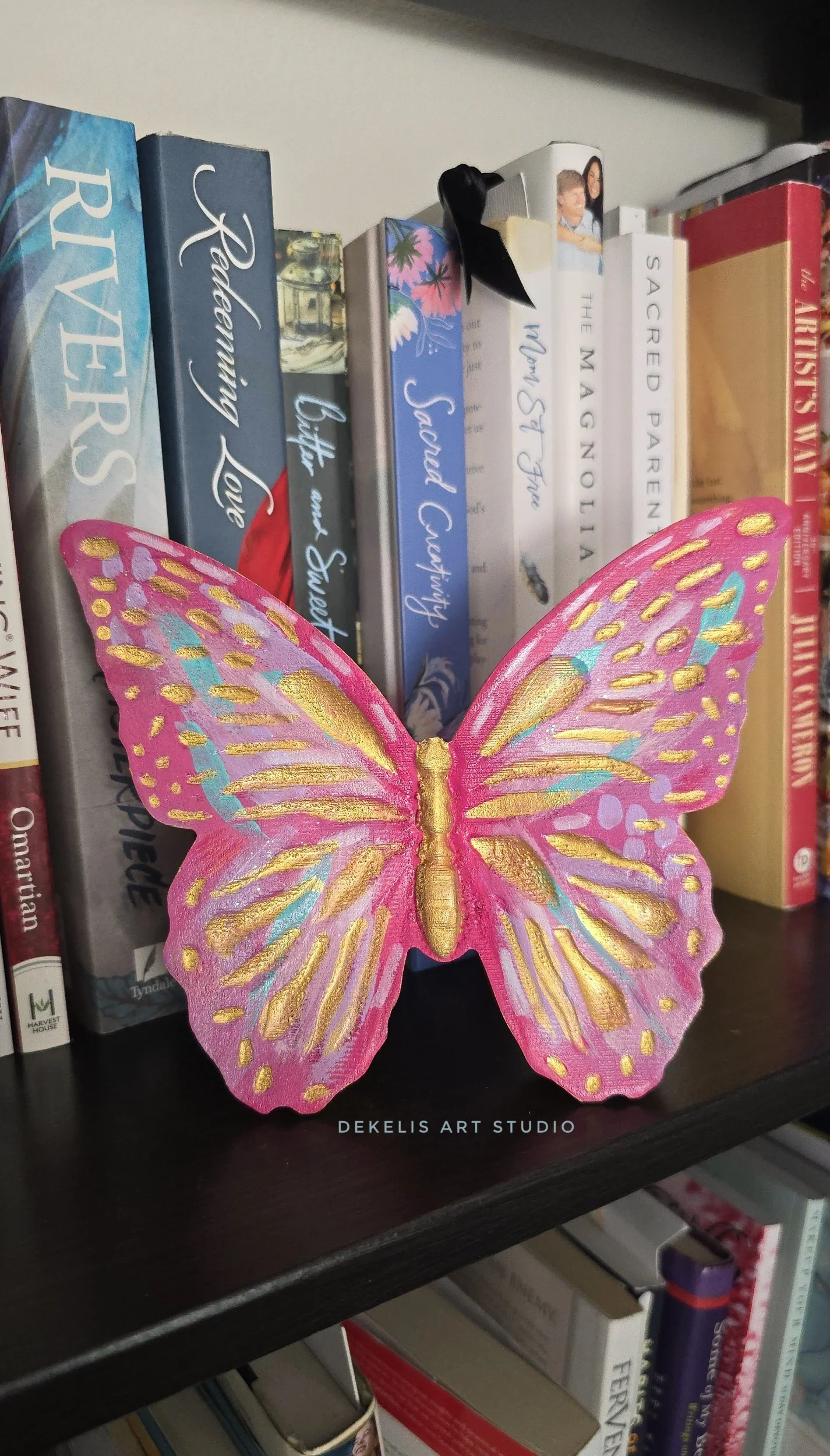 Brighten any space with this hand-painted wooden butterfly, finished in shimmering metallic gold, sweet pink, lavender, turquoise and white.