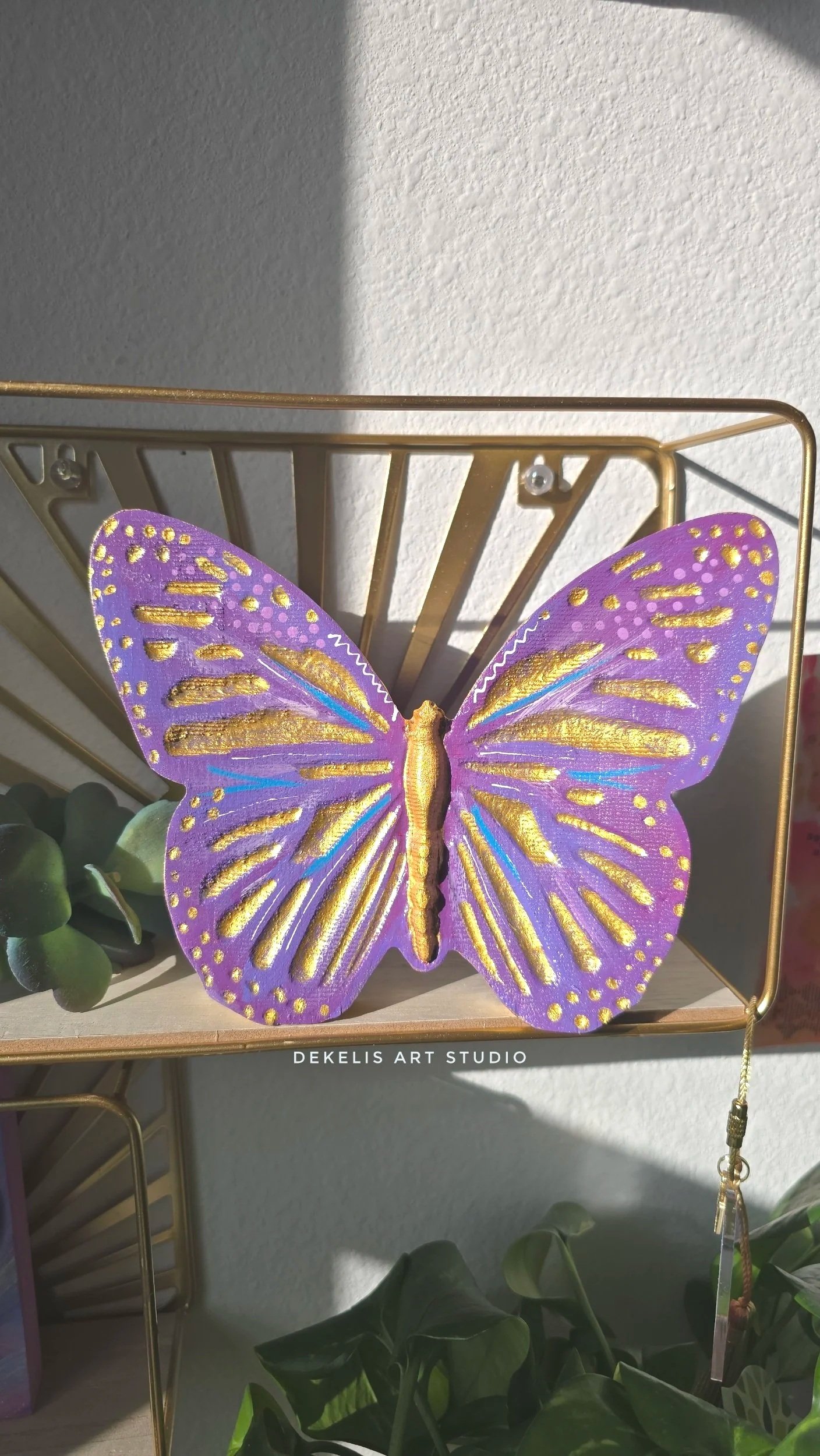 Brighten any space with this hand-painted wooden butterfly, finished in shimmering metallic gold, rich purple, blue and white.