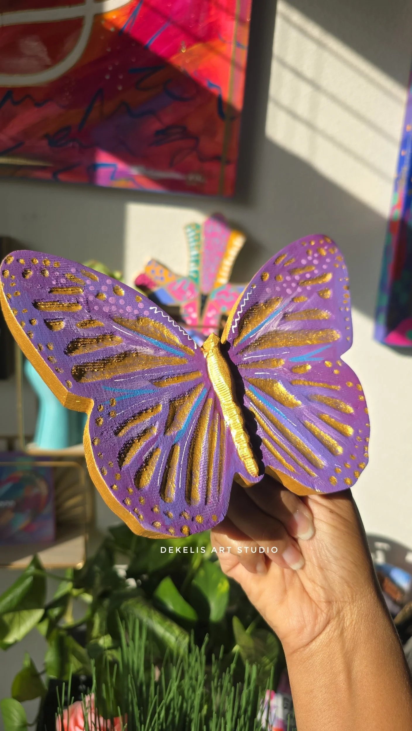 Brighten any space with this hand-painted wooden butterfly, finished in shimmering metallic gold, rich purple, blue and white.