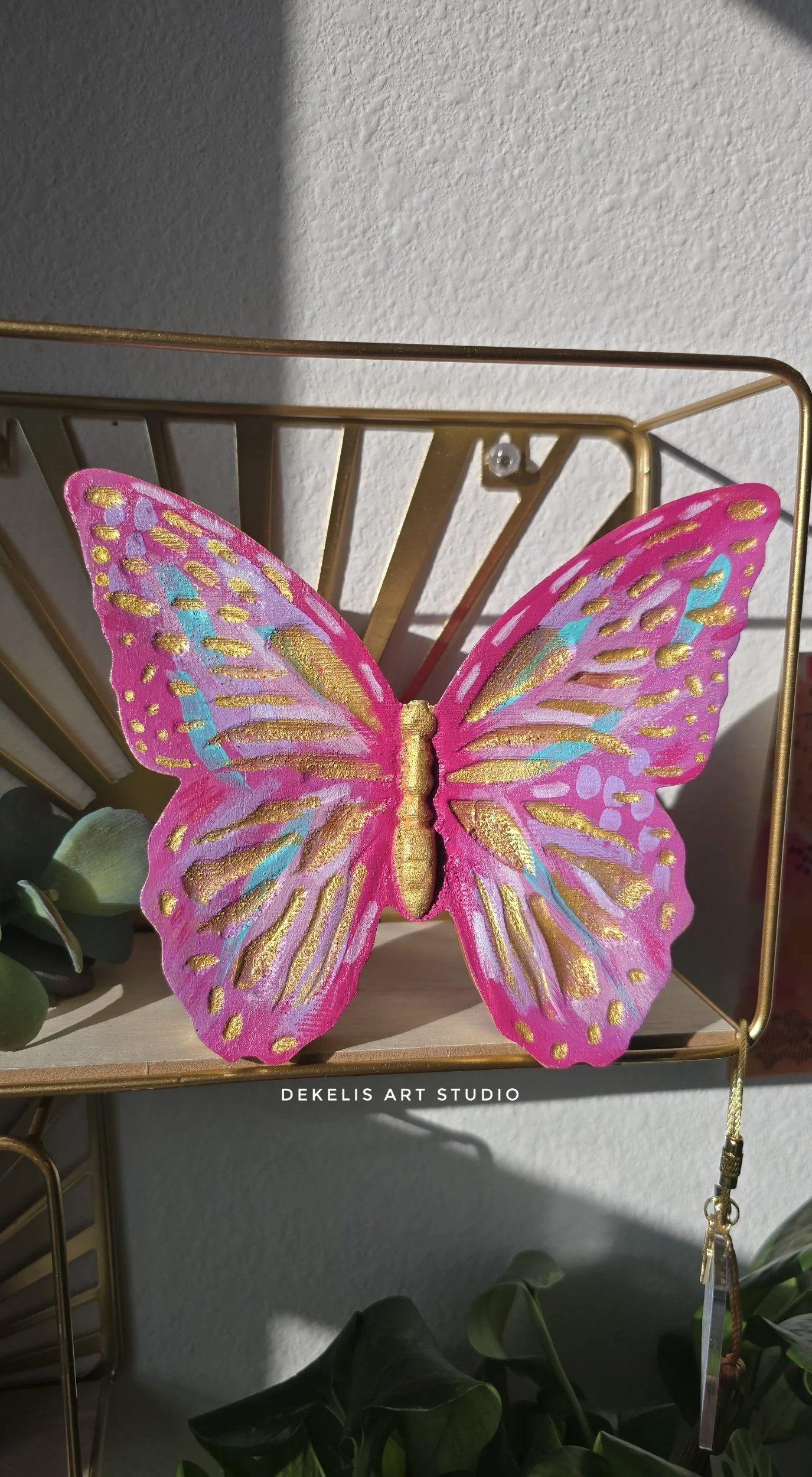 Brighten any space with this hand-painted wooden butterfly, finished in shimmering metallic gold, sweet pink, lavender, turquoise and white.