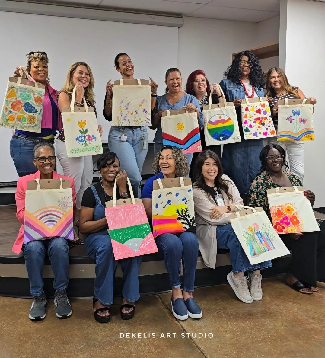 Group of women from Healthy Start Coalition posing with their hand-painted totebags completed during an in-house art and work stress management workshop led by Desirae Ofori of DeKelis Art Studio