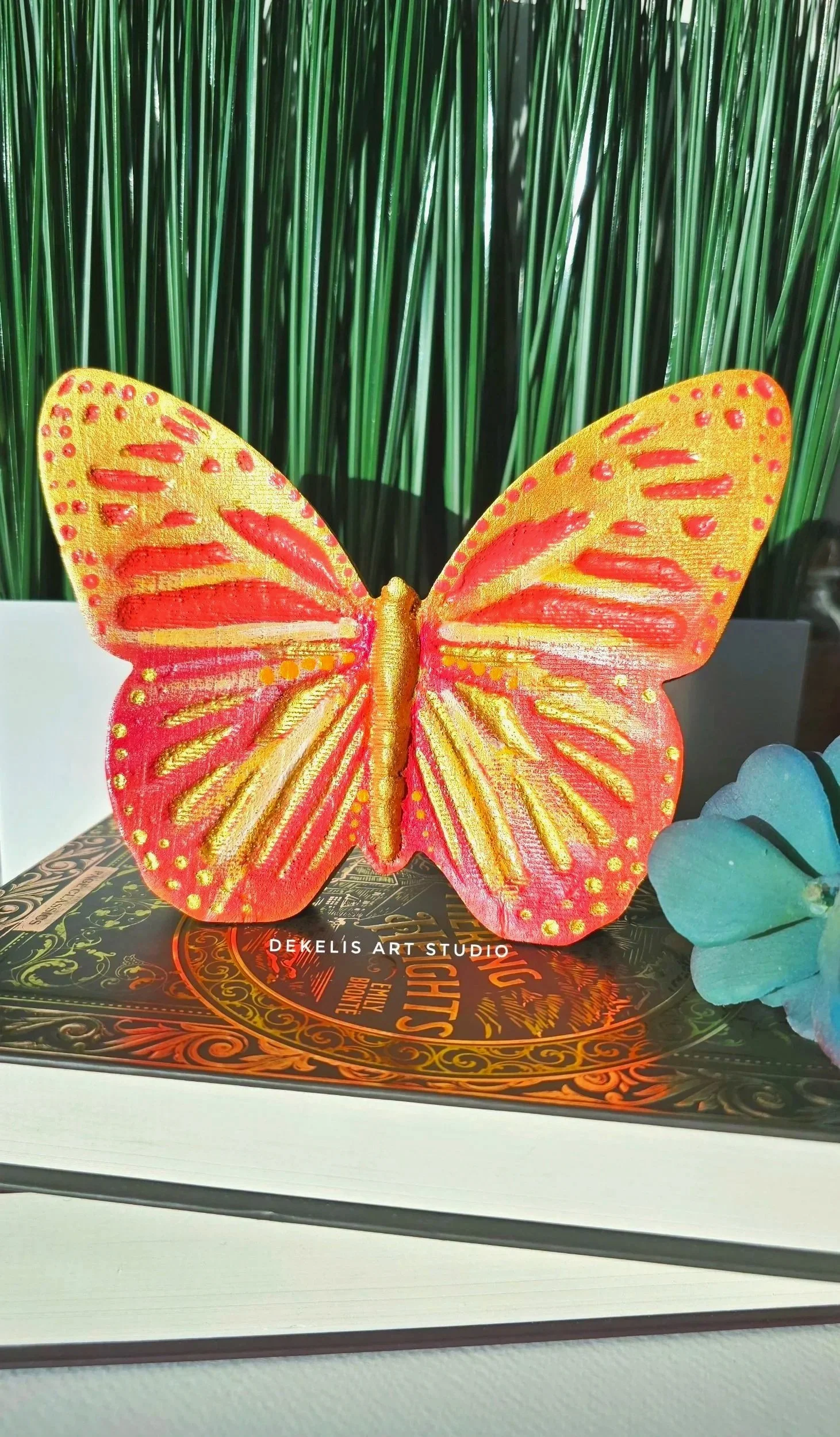Brighten any space with this hand-painted wooden butterfly, finished in shimmering metallic gold, warm orange, coral, soft yellow and white.
