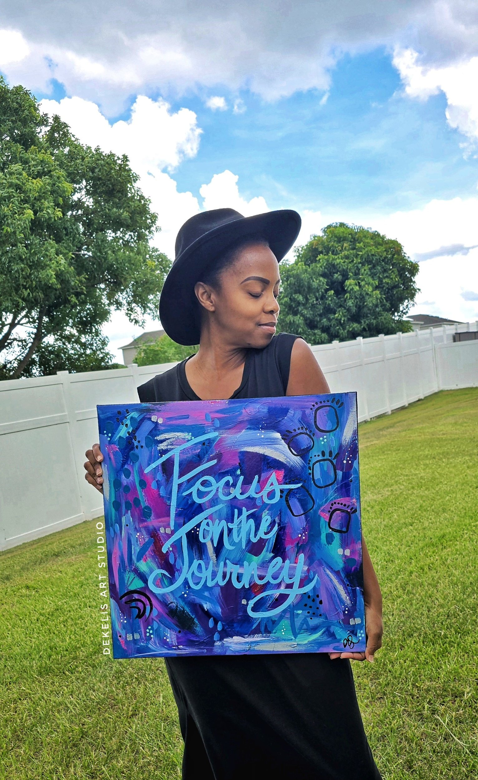Black woman wearing a black hat holding an inspirational maximalist abstract painting