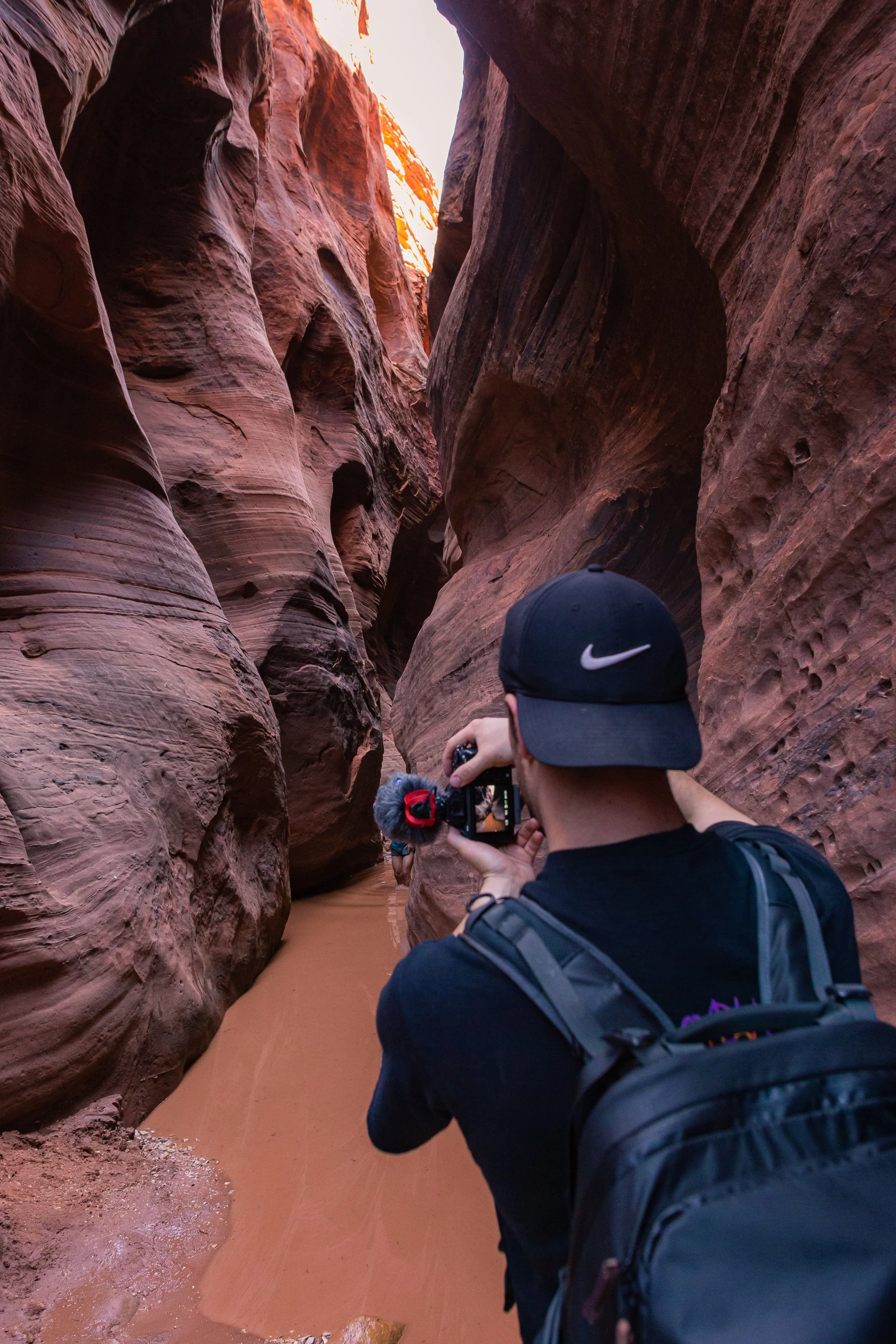 a photographer holding a camera as he looks down Buckskin Gulch canyon and takes a photo