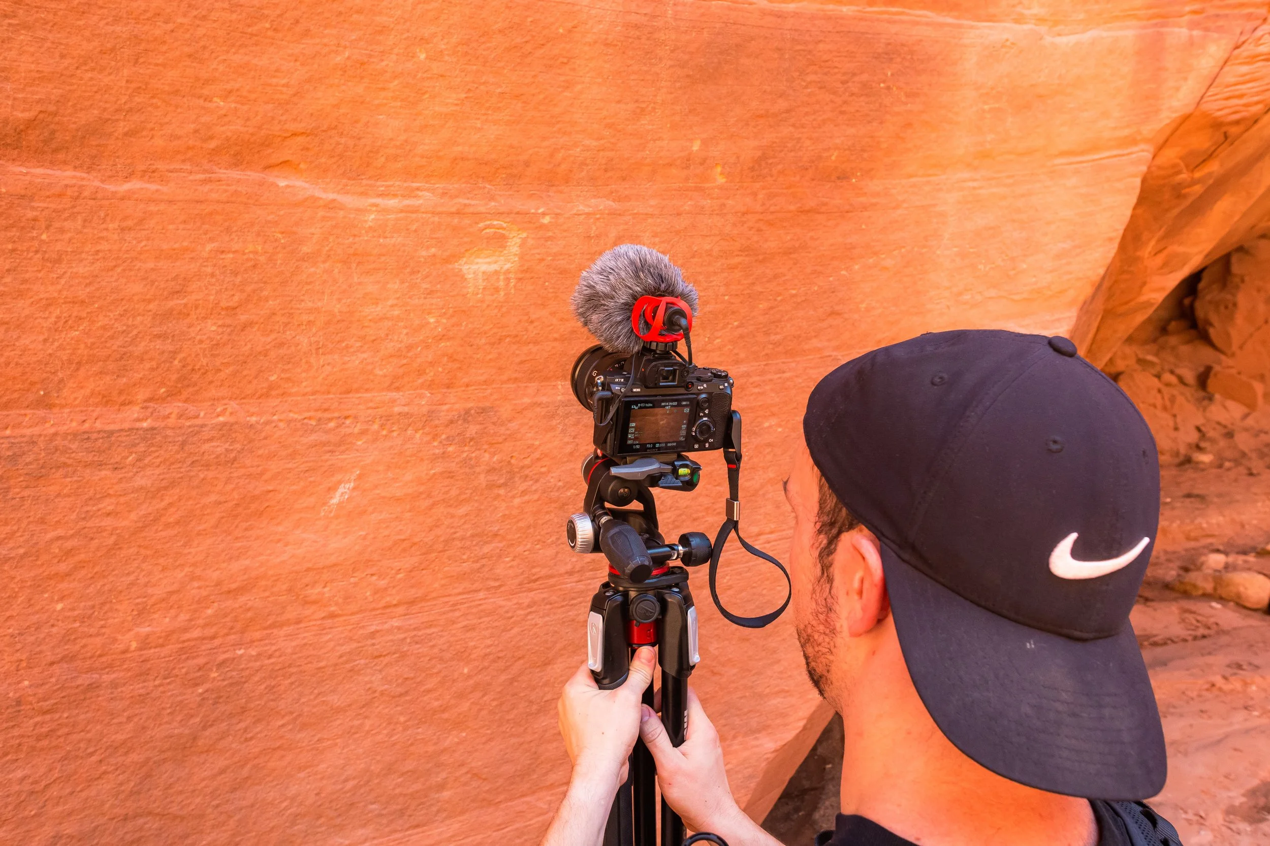 A photographer holding up a camera with a mic on it to record petroglyps on desert canyon walls