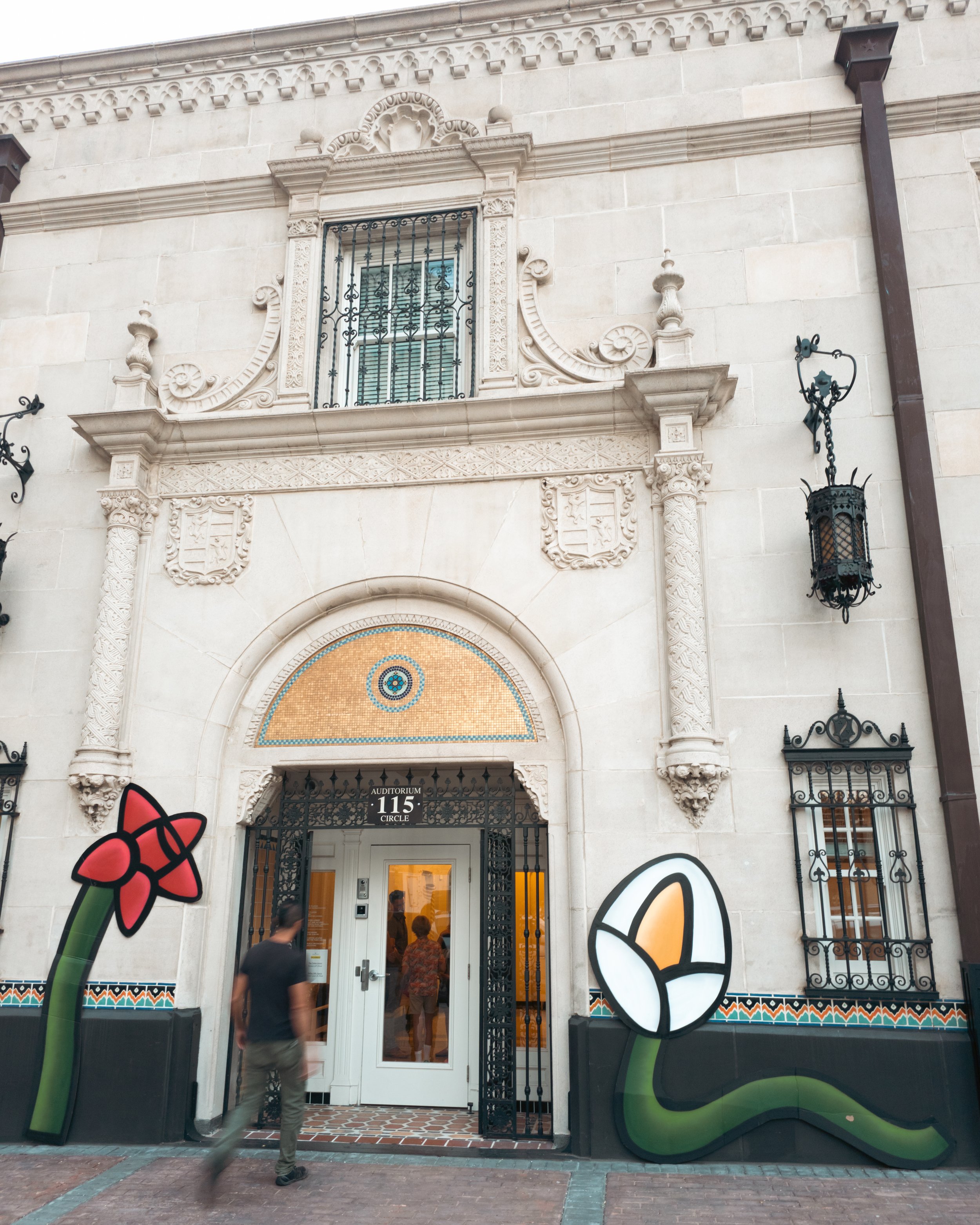 A man walks into the entrance of a building which has a wabi sabi painting by Albert Gonzalez on each side.