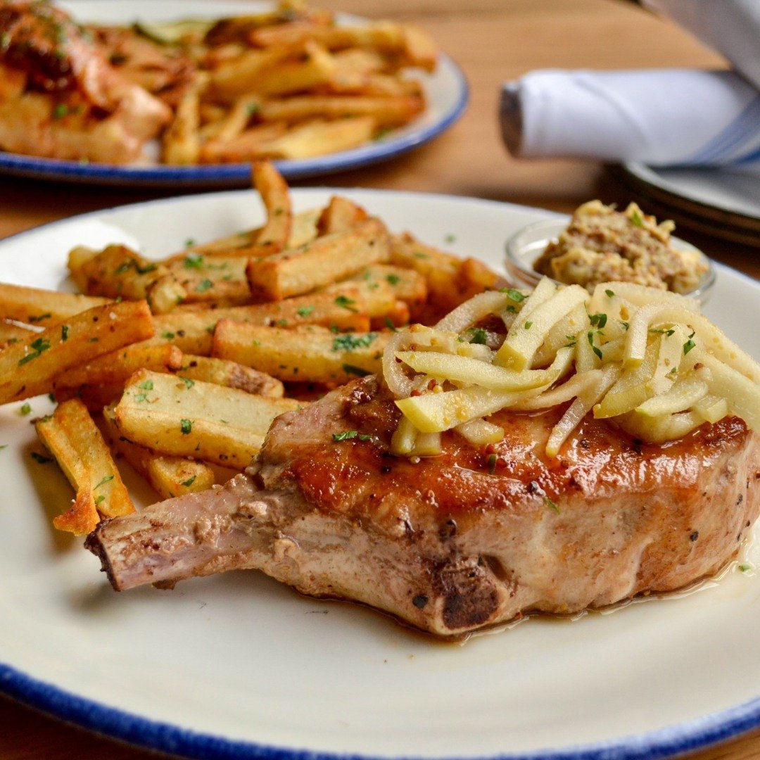 Tender and tasty 🍽️😋 Our Grilled Pork Chop is served with roasted apple and whole grain mustard, pickled apples, fresh cut fries. Yum! 🍖