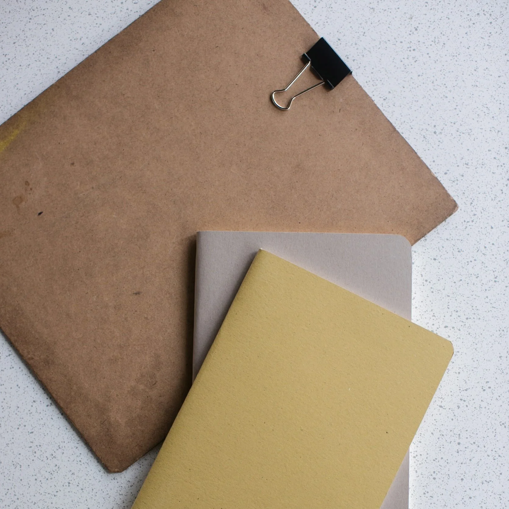 Stack of brown envelope with paper clip on top and two notebooks
